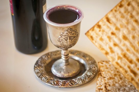 Red wine, a cup full of wine with the text of the traditional wine blessing "Borei Pri HaGafen" ("Blessed is the fruit of vine") and matzot. Passover seder set stock image blurred. Israel, April 2016.