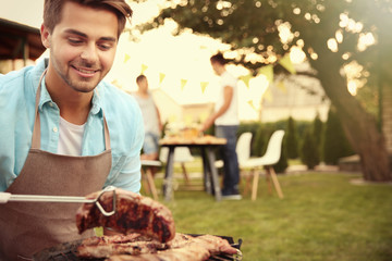 Handsome young man preparing barbecue steaks on grill
