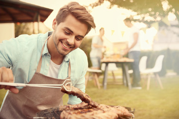 Handsome young man preparing barbecue steaks on grill