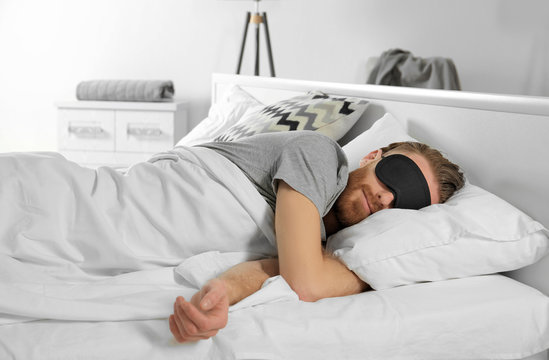 Handsome man sleeping with blindfold in bed at home
