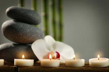 Fototapeta na wymiar Spa still life with pebbles, candles and orchid flower on grey background
