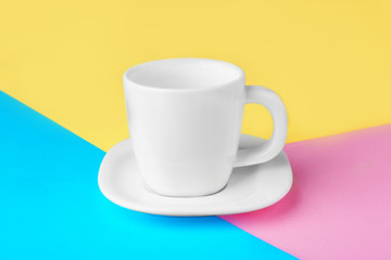 Blank ceramic cup with saucer on color paper background