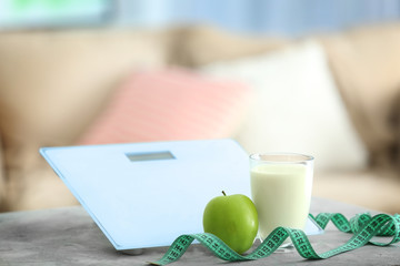 Glass of milk, apple, measuring tape and scales on kitchen table