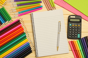 Plakat blank paper notebook with colored pencils, pains, calculator for school and student education on wood background