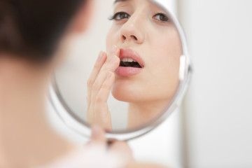 Young woman with cold sore looking in mirror at home - obrazy, fototapety, plakaty