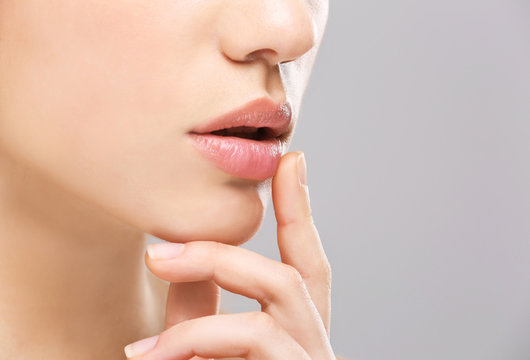 Woman with cold sore touching lips on light background