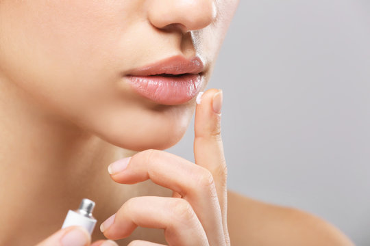 Beautiful woman applying cream onto lips on light background