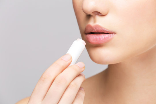 Woman applying hygienic lip balm on light background