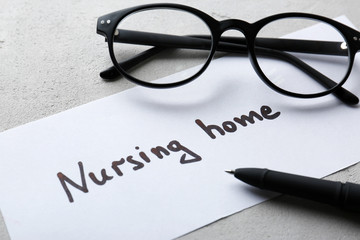 Eyeglasses and paper sheet with text NURSING HOME on light background