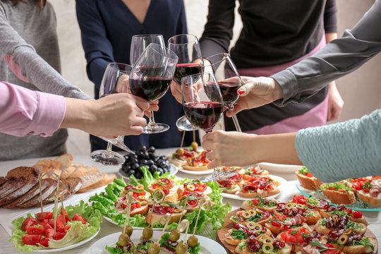 People clinking glasses with wine and delicious dishes on table