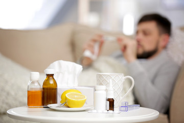 Medicines, cup of hot tea and lemons with blurred ill man on background