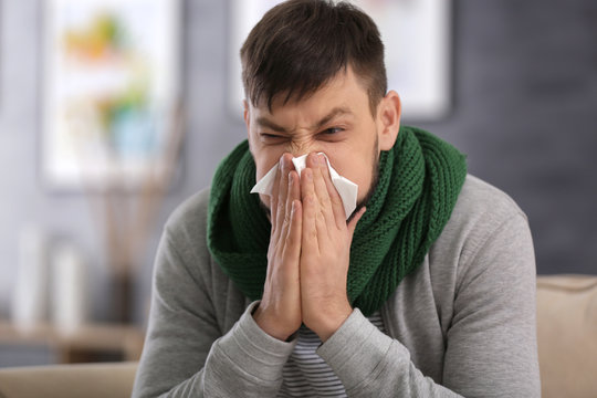 Young ill man blowing nose at home
