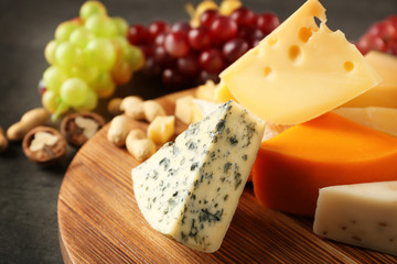 Wooden board with cheese, grape and nuts on grey background