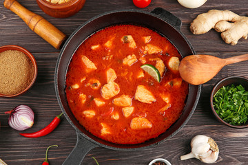 Delicious chicken tikka masala in pan and spices on wooden table