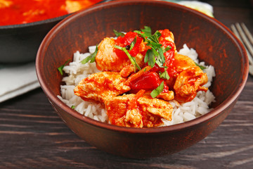 Portion of chicken tikka masala and rice in bowl on wooden table