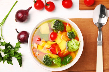 Bowl with delicious soup and vegetables on kitchen table