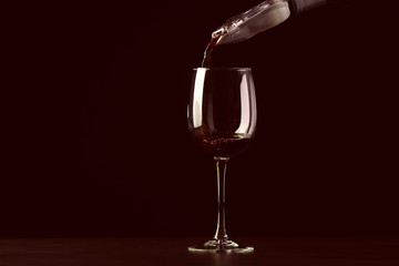Pouring red wine into glass on dark background