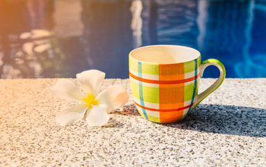 Colorful cup of coffee on the edge of pool.