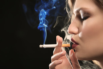 Obraz premium Portrait of beautiful woman with cigarette on black background