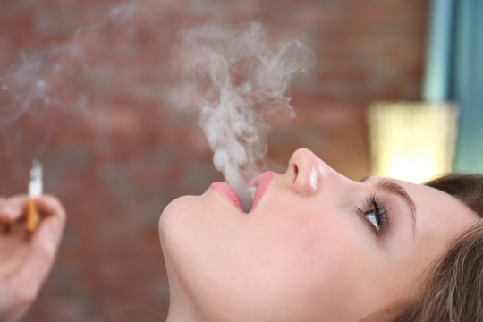 Young woman smoking on blurred background
