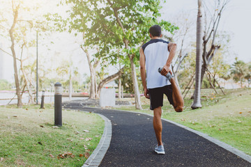 Young man stretching bodies, warming up for jogging in public park.