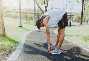 Young man stretching bodies, warming up for jogging in public park.