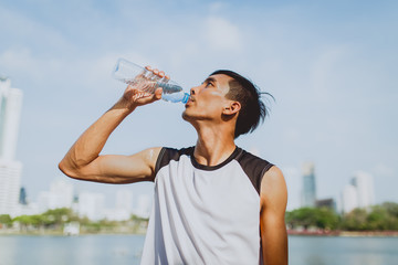 Sports man drinking water after exercising on background of public park.