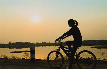 Fototapeta premium Silhouette biker-girl at the sunset on the meadow