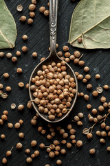 Dry coriander seeds in metal spoon on a black wooden table, top view