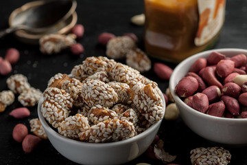 Peanuts in ceramic bowls and jar with caramel on a wooden table, selective focus