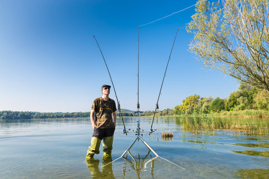 Fishing adventures. Fisherman and carp fishing gear. Angler with green waders on lake, near the carpfishing equipment in a sunny day