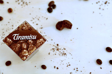Top view of tiramisu glass and coffee beans, cocoa powder, chocolate pieces on light brown, wooden background
