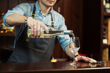 Male sommelier pouring white wine into long-stemmed wineglasses.
