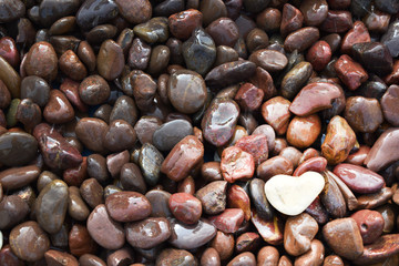A white heart shaped stone in bottom right of frame  resting on a brown stone pebble variety and with space for your copy.