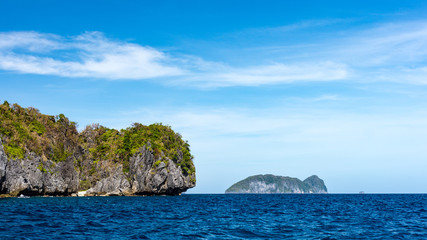 Fototapeta na wymiar Distant view across a calm blue sea of some small rocky islands around El Nido, Philippines.
