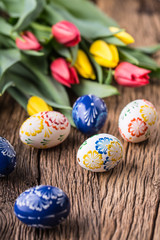 Easter. Hand made easter eggs and spring tulips on old wooden table.