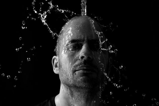 Portrait of a man being thrown water in the face against a black background