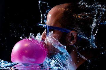 Portrait of a man with sun glasses chewing gum and being thrown water in the face against a black background 