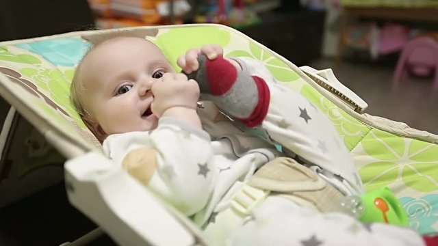 Cute baby lying in a children's rocking chair and tries to lift his sock.