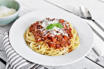 Spaghetti Bolognese on a white plate with decorative basil leaf. Italian cuisine, pasta with tomato sauce and parmesan cheese.