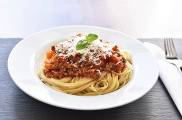 Spaghetti Bolognese on a white plate with decorative basil leaf. Italian cuisine, pasta with tomato sauce and parmesan cheese.