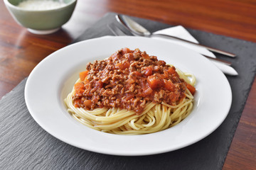 Spaghetti Bolognese on a white plate with decorative basil leaf. Italian cuisine, pasta with tomato sauce and parmesan cheese.