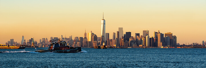 Fototapeta na wymiar Panoramic Sunset of Lower Manhattan and New York City Harbor with Financial District skyscrapers and passing tugboat