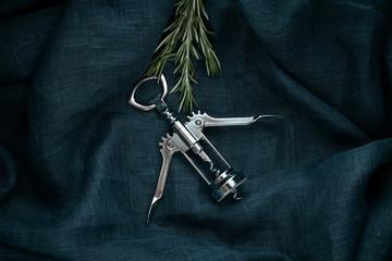 Kitchen accessory. Metal bottle opener with  rosemary on textile background.