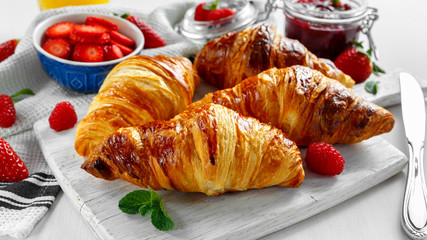 Fresh tasty homemade croissants with ripe berries and raspberries jam on white wooden board