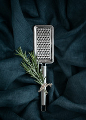Kitchen accessory. Metal cheese grater with rosemary on textile background.
