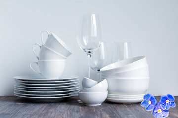 White dishware stacked on a wooden table against white background with transparent wineglasses