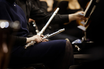 Flute in the hands of a woman in an orchestra in dark tones - obrazy, fototapety, plakaty
