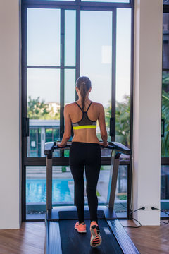 Woman running on the treadmill in the gym with a great poolside view