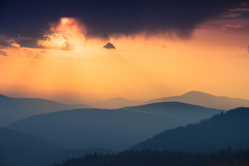 Fantastic sunrise above peaks of smoky mountain with the view into misty hills. Dramatic overcast sky. Mountains silhouettes.